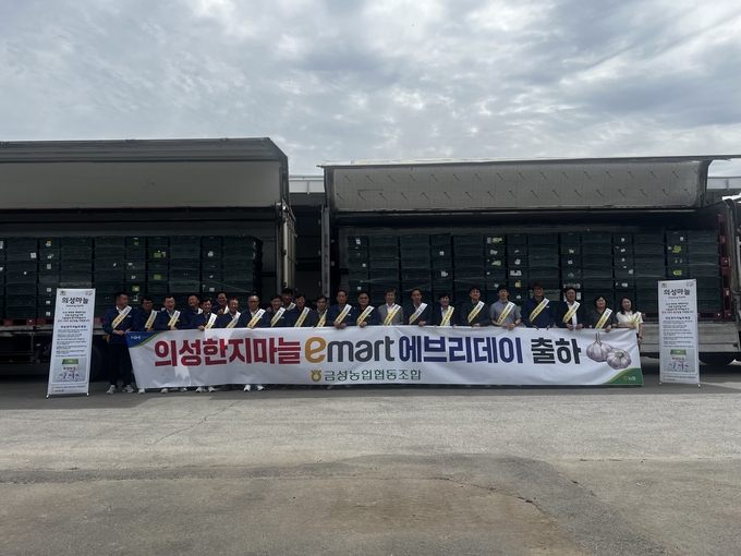 ▲ 6월 24일 경북 의성군 금성농협 경제사업장에서 조용일 조합장(오른쪽 여덟 번째)과 장승연 의성군농업기술센터 소장(아홉 번째)을 비롯한 임직원들이 ‘의성 한지마늘 이마트 에브리데이 출하 기념식’을 열고 전국 매장으로 출하되는 의성마늘 운송차량 앞에서 현수막을 펼쳐 들고 기념촬영을 하고 있다. 의성군 금성농협 제공