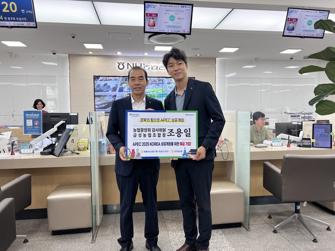 ▲ 9월 4일 경북 의성군 NH농협은행 의성군지부 영업점에서 조용일 농협중앙회 감사위원(금성농협 조합장·왼쪽)과 이진석 지부장이 ‘APEC 2025 KOREA 성공개최 기원 예금’ 가입을 마친 뒤 창구 앞에서 인증 현수판을 들고 미소를 지으며 기념촬영을 하고 있다. 금성농협 제공